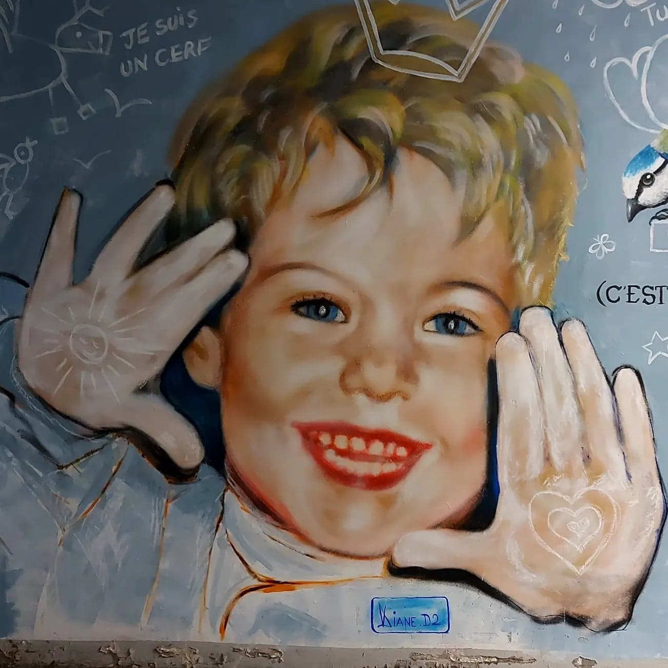 Fresque murale : portrait d’un enfant blond, les mains ouvertes de part et d’autre du visage